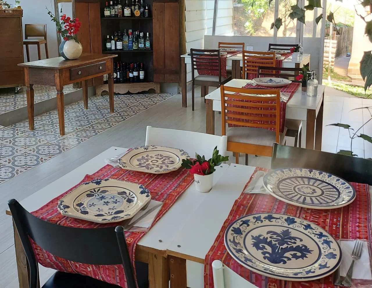 Mesas do Salão Provençal postas com pratos pintados em azul e branco sobre caminhos de mesa vermelhos